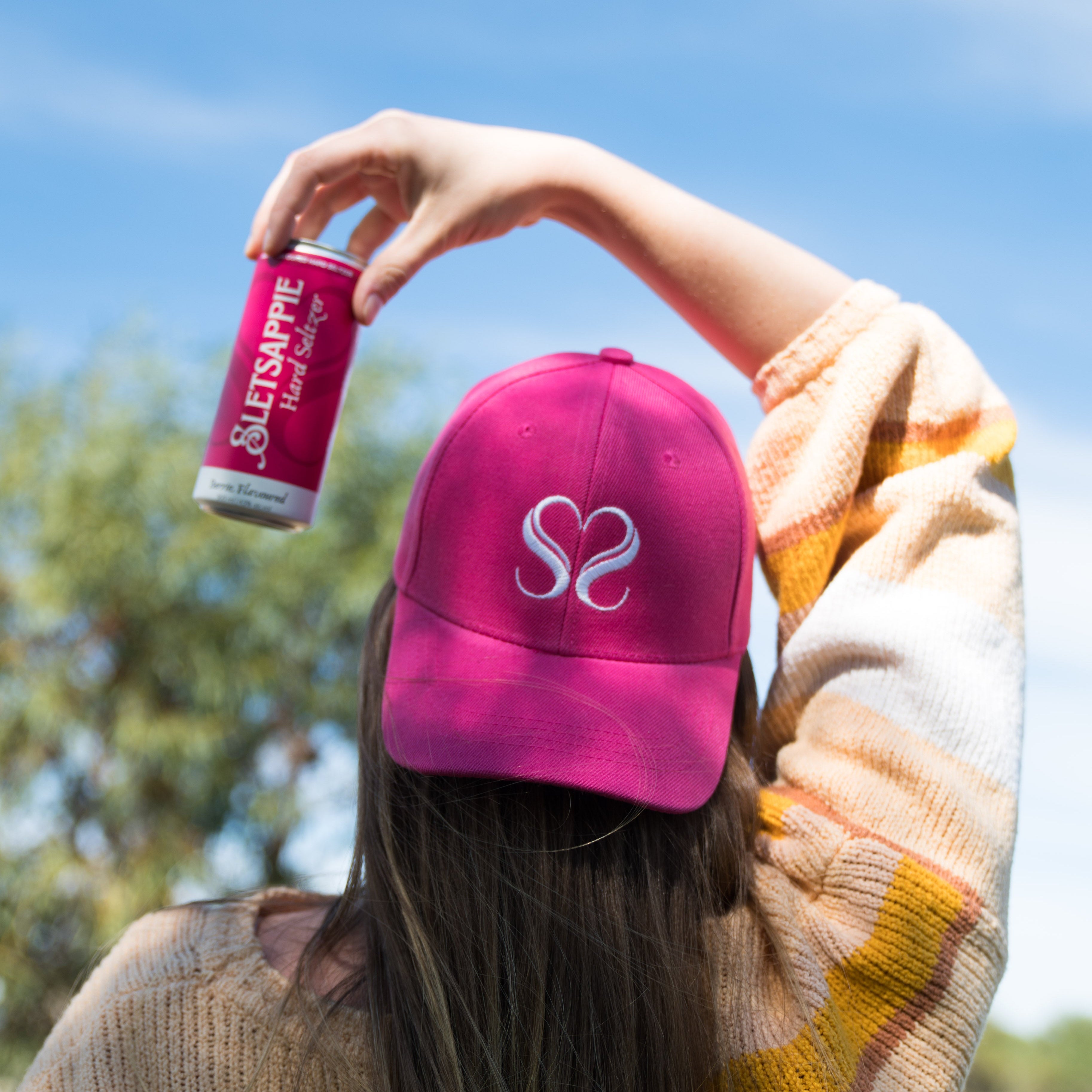 Person wearing a pink cap with a logo and holding a can against a blue sky.